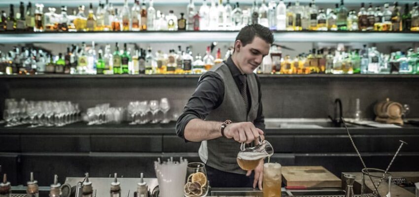 Barman en cravate versant un cocktail derrière le bar.
