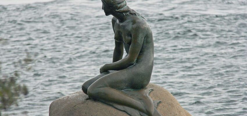 Une statue de sirène assise sur un rocher.