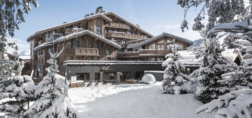 Chalet enneigé entouré d'arbres sous ciel bleu.