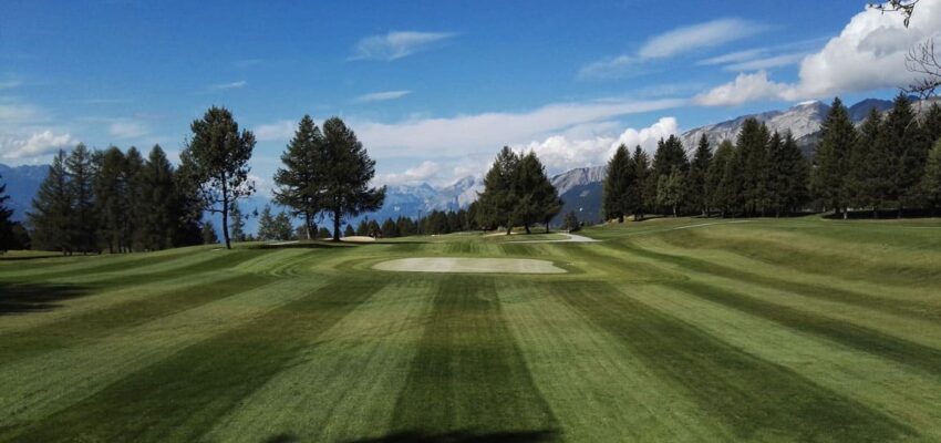 Terrain de golf : pelouse verte rayée, bunker au centre.