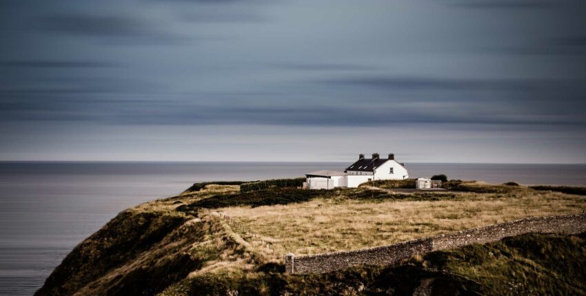 Maison isolée sur falaise avec vue sur mer.