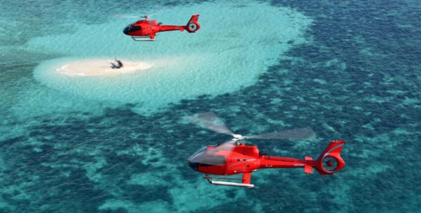 Location jet privé, hélicoptères survolant île sableuse et eau turquoise.