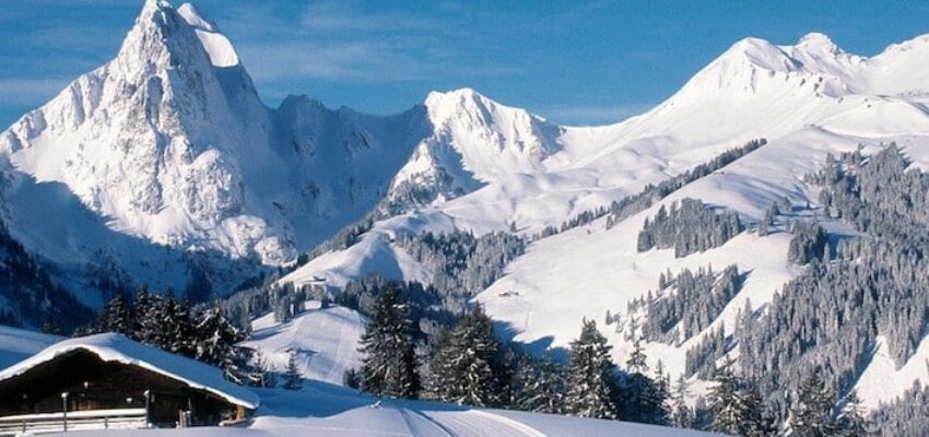 Paysage montagneux enneigé avec cabane en bois et ciel.
