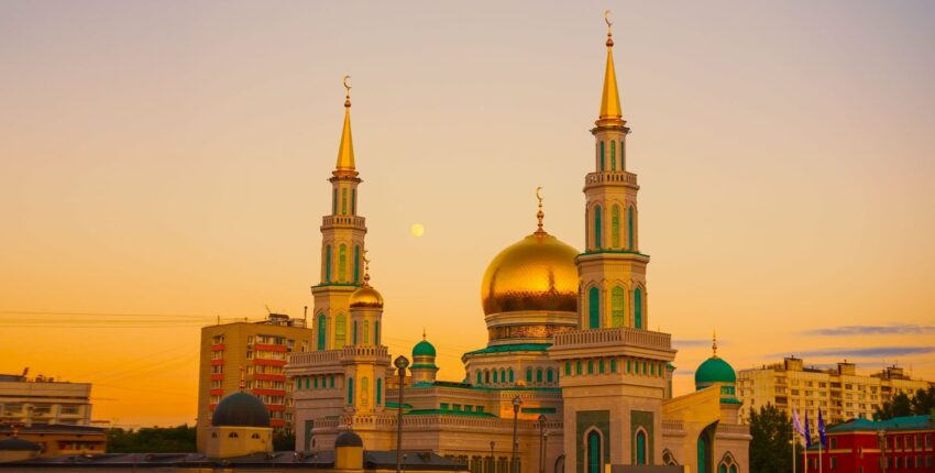 Coucher de soleil sur la mosquée, dômes dorés, grands minarets, ciel clair.