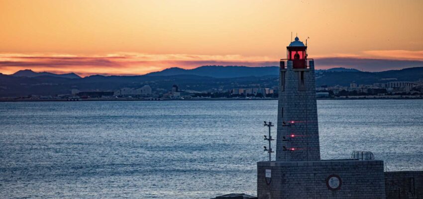 Phare au bord de la mer au coucher du soleil coloré avec des montagnes.