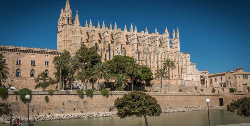 Cathédrale gothique, flèches, palmiers reflétés dans la rivière.