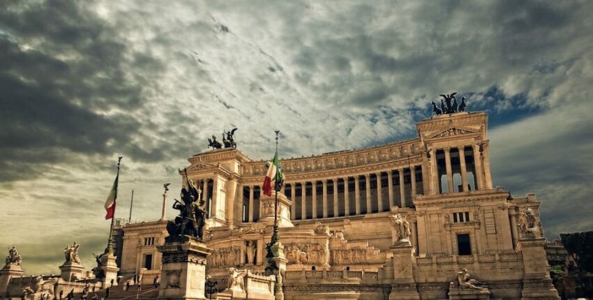 Bâtiment historique, architecture ornée, colonnes, personnages, drapeaux italiens.