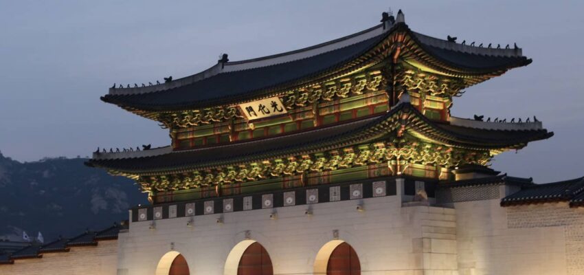Porte illuminée du palais de Gyeongbokgung avec des piétons au crépuscule.