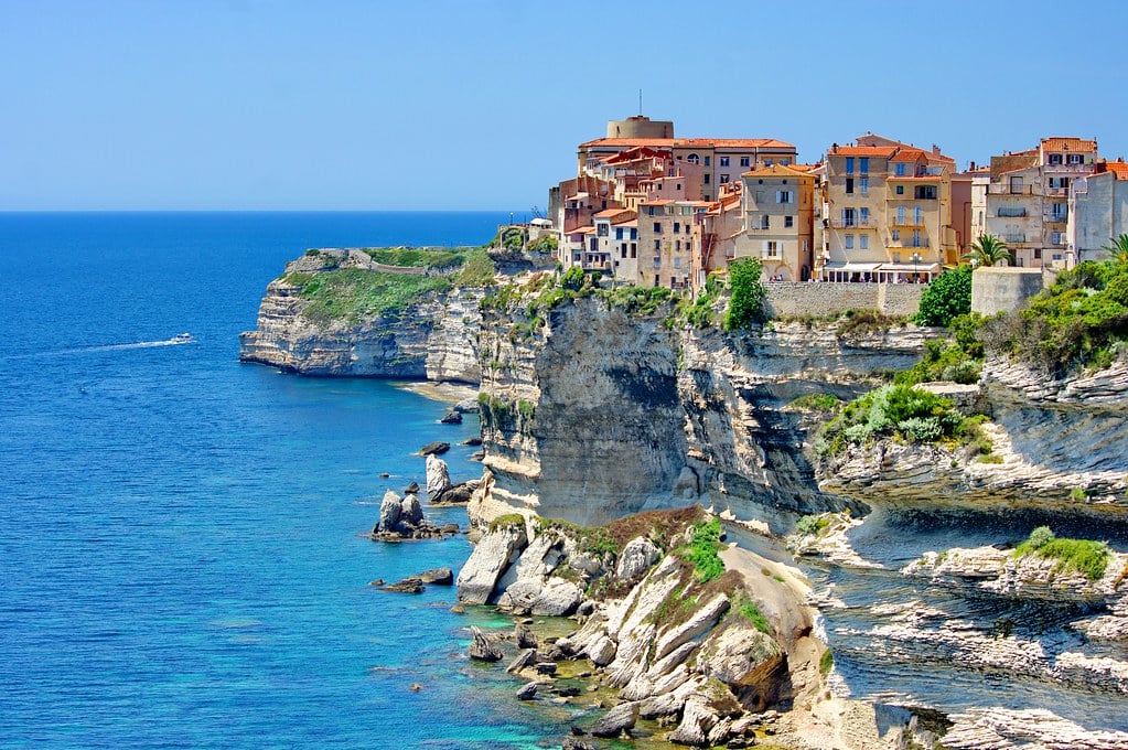 **Texte alternatif :** Corse : Ville colorée, mer bleue, et bateau en-dessous.