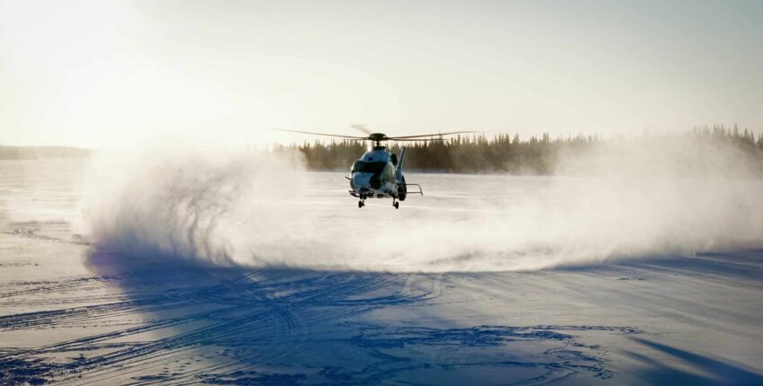 Hélicoptère H160 planant près du sol enneigé.